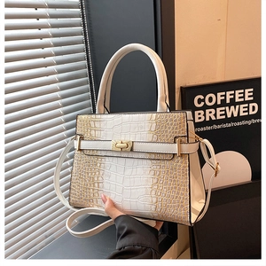Detail of white crocodile-embossed tote bag featuring a gold lock and structured top handle