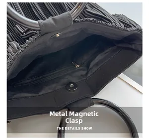 Detail view of the black pleated bag interior featuring a metal magnetic buckle and zipper pocket