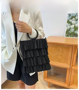 Detail of black pleated bucket bag with resin ring handle on a model in a white blazer