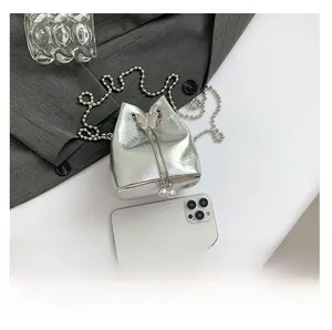Silberne Metallic-Beuteltasche mit rosa Schmetterling neben einem Smartphone im Vergleich