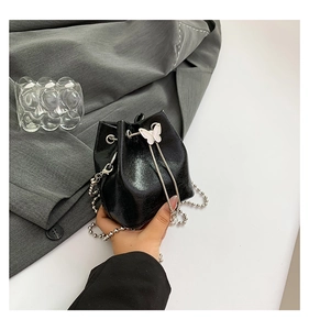 Detail der schwarzen glänzenden Beuteltasche mit weißer Schmetterlingsschnalle und Perlenkette