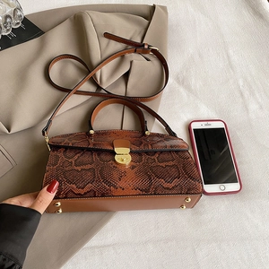 Brown snakeskin tote bag with top handle and gold turn-lock closure on a brown blazer
