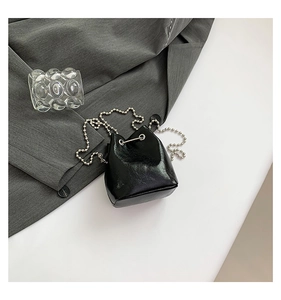 Detail einer Mini-Eimertasche in Schwarz mit glänzender Lederoptik und silberner Kugelkette