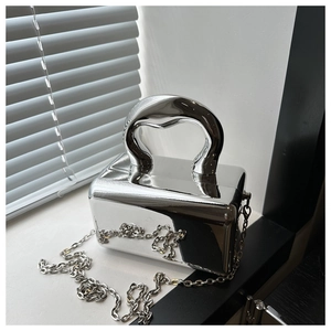 Macro detail of silver mirror acrylic box bag with metallic handle and chain strap