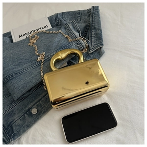 Detail of gold mirror acrylic clutch bag with round metal handle and chain on white fabric