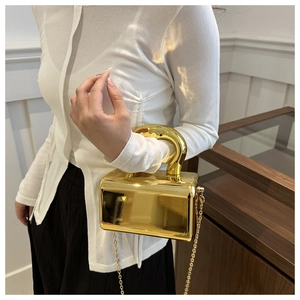 Close-up of golden mirror acrylic box bag featuring a chunky round metal handle