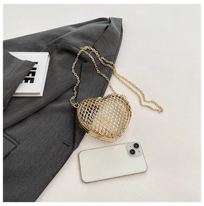 Gold heart-shaped hollow metal evening bag with chain strap placed on a grey blazer