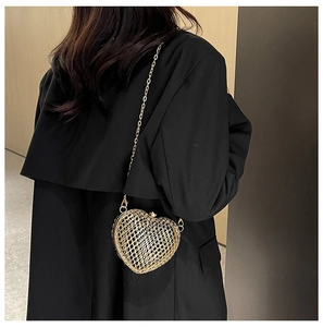 Detail view of heart-shaped gold woven metal chain bag worn across the back over dark clothing