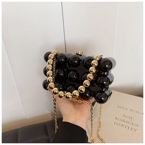 Detail of a black beaded evening bag with decorative gold ball chain and metal strap