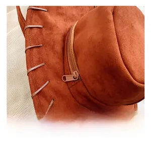 Close-up of the metal zipper hardware and woven trim on a caramel suede hat backpack