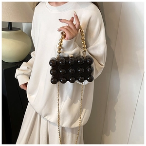 Close-up of black bubble textured handbag with gold bead handle and metallic chain strap