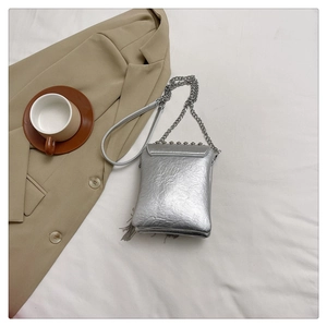 Detail of silver textured mini crossbody bag with metal chain on white fabric background
