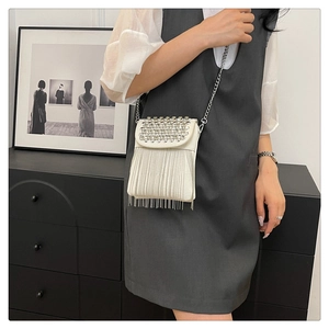 Close-up of white crossbody bag with silver studs and long metal chain tassels detail
