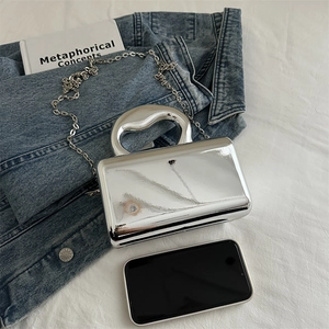 Silver mirror acrylic mini handbag with heart handle and chain strap on denim background