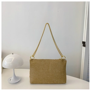 Detail view of woven envelope chain bag with golden ring hardware on white table