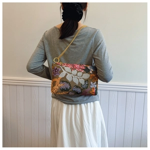 Detail of vintage embroidered floral shoulder bag with sequins and gold chain strap on model