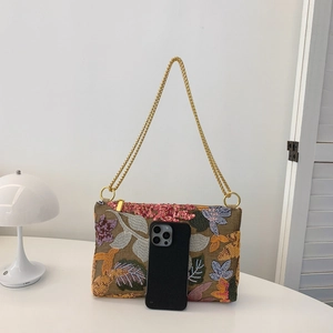 Floral embroidered envelope chain bag with pink sequins and gold strap on white table