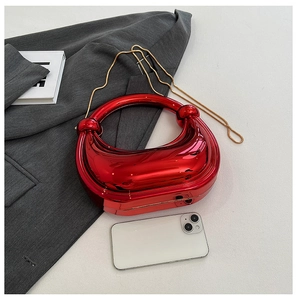 Détail d'un sac demi-lune rouge métallisé avec chaîne dorée sur une veste grise