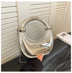 Détail d'un sac demi-lune argenté avec poignée anneau et chaîne porté sur un canapé