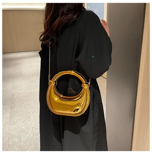 Détail d'une pochette en acrylique miroir doré tenue par un mannequin en manteau noir