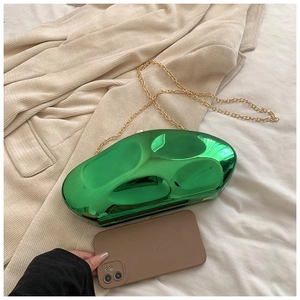 Close-up of green pebble-shaped acrylic clutch bag with gold chain on stylish fabric