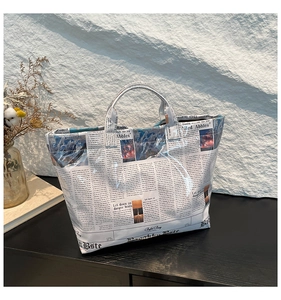 Detail of a newspaper print tote bag with a glossy finish and durable top handles