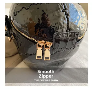 Detail of smooth gold double zippers on black glossy wave textured crossbody bag