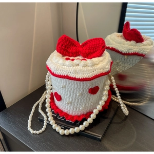 Détail d'un sac seau tricoté en forme de gâteau avec nœuds rouges et chaîne perlée
