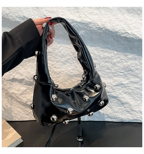 Détail d'un sac hobo noir brillant avec clous argentés et bandoulière tenu à la main