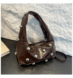 Gros plan détaillé du sac en cuir verni marron foncé avec des clous métalliques argentés