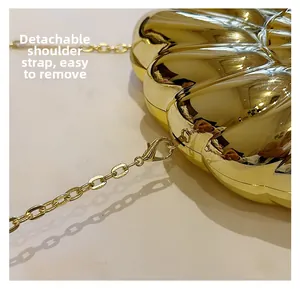 Détail de la bandoulière chaîne dorée amovible sur un sac pochette en métal en forme de coquille