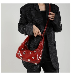 Gros plan d'un sac en cuir verni rouge à rivets argentés sur un blazer noir