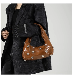 Détail des rivets argentés sur un sac demi-lune en cuir verni caramel porté par un modèle