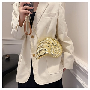Détail d'une pochette coquillage dorée métallisée avec chaîne sur une tenue chic