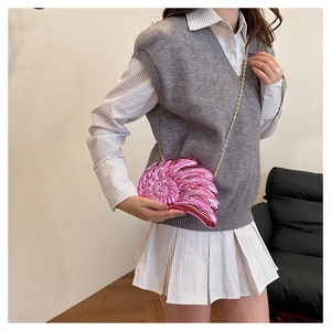 Sac bandoulière coquillage rose métallisé chic avec chaîne dorée porté par un mannequin