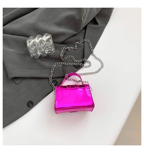Detail of a shiny magenta mini square flap bag with silver chain strap on gray fabric