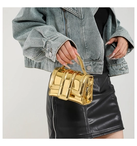 Detail of a mini gold crossbody bag with metallic mirror finish and buckle straps