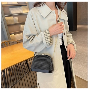 Detail of a black shell crossbody bag with acrylic gold chain on a trench coat