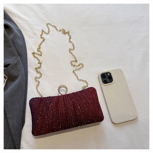 Detail of burgundy glitter evening clutch with crystal clasp and gold chain beside a phone