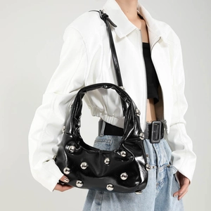 Sac sous le bras chic en cuir verni noir avec rivets argentés porté par un modèle