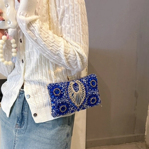Blue rhinestone evening bag with gold chain strap shown on white knit cardigan