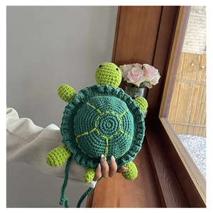 Close-up of handmade green knit turtle crossbody bag with yellow shell embroidery