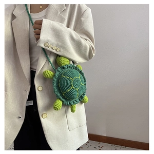 Detail of cute green turtle crochet bag showing hand-knitted texture and strap on a model