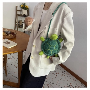 Detail of a handmade green turtle-shaped knitted crossbody bag worn by a model in a cozy room