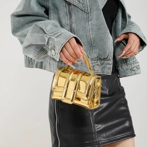 Mini gold metallic square crossbody bag with handle shown in a modern studio setting