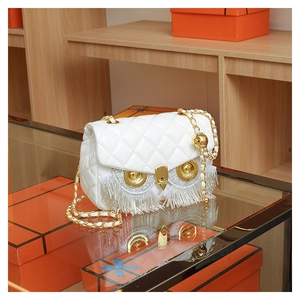 Detail of white quilted handbag with owl metallic eyes and golden chain strap