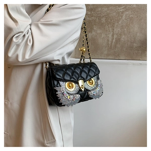 Detail of black quilted shoulder bag with owl rhinestone design and gold chain strap