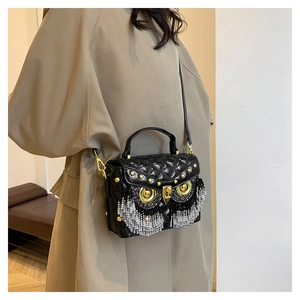 Close-up of owl-shaped black quilted handbag with crystal eyes and beaded tassels