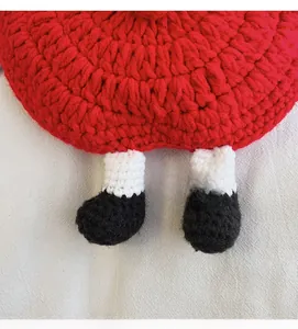 Close-up of handmade red crochet apple bag featuring cute cartoon feet and soft knitted texture