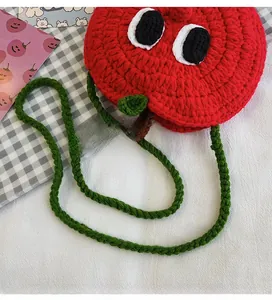 Close-up of handmade red apple knit bag with green shoulder strap and cute eye details